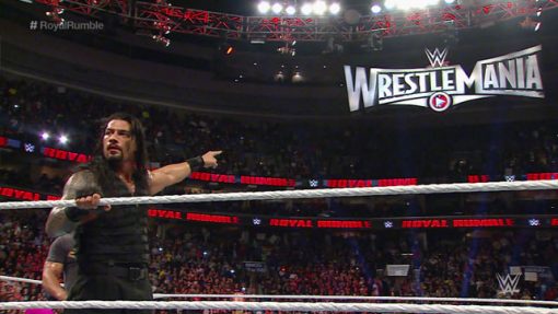 Roman Reigns pointing at Wrestlemania sign